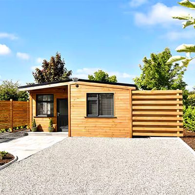 Timber cabin with a flat gravel drive and a horizontal timber fence, in summer