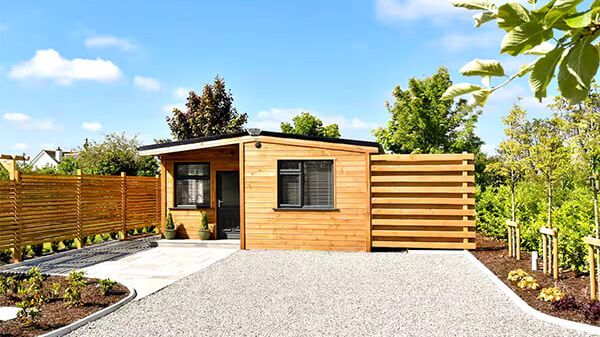 Timber cabin with a flat gravel drive and a horizontal timber fence, in summer
