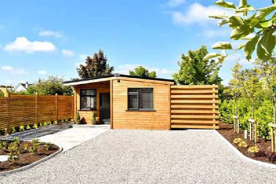Timber cabin with a flat gravel drive and a horizontal timber fence, in summer